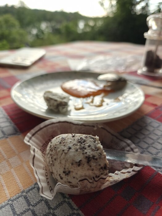 Tryffelgetost på rutig duk utomhus, med sked och marmelad på en tallrik i bakgrunden.