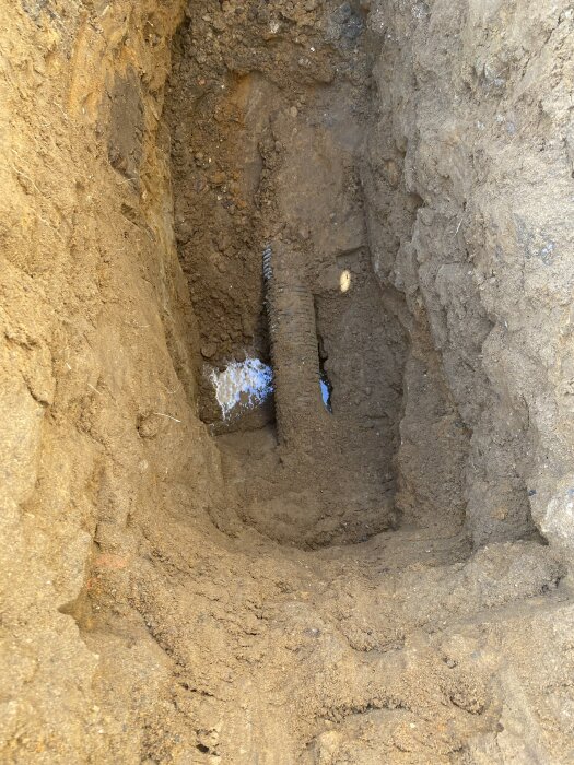 Ett äldre dräneringsrör syns i en utgrävd grop i marken, där vatten rinner ut från rörets mynning.