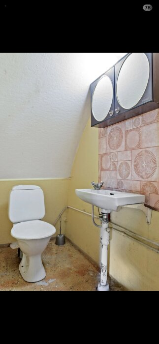 Källartoalett med beige väggar, vitt handfat, spegelskåp, och ficklampa på golvet. Vit toalettstol placerad mot väggen.