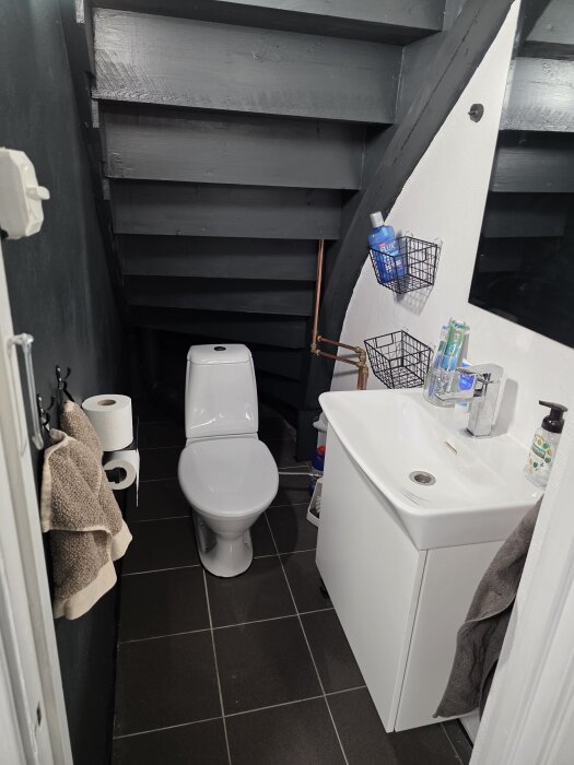 Renoverad källartoalett med nytt golv, vit handfat och förberedd för badrumsrenovering på övervåningen. Inget toalock på plats.