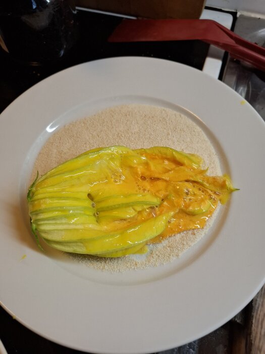 En squashblomma fylld med gul fyllning, placerad på en tallrik med ett lager av ströbröd.
