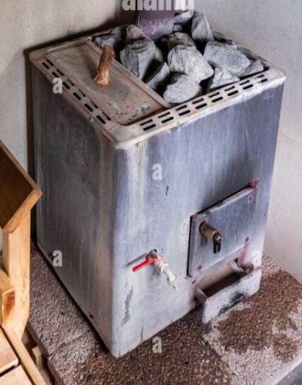 Äldre vedeldad bastukamin med tappkran, omgiven av stenar. Vid sidan står en träbänk.