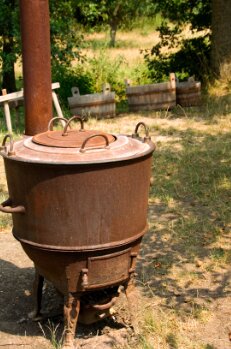 Rostig vedeldad bykgryta i trädgårdsmiljö, använd för varmvattenuppvärmning.