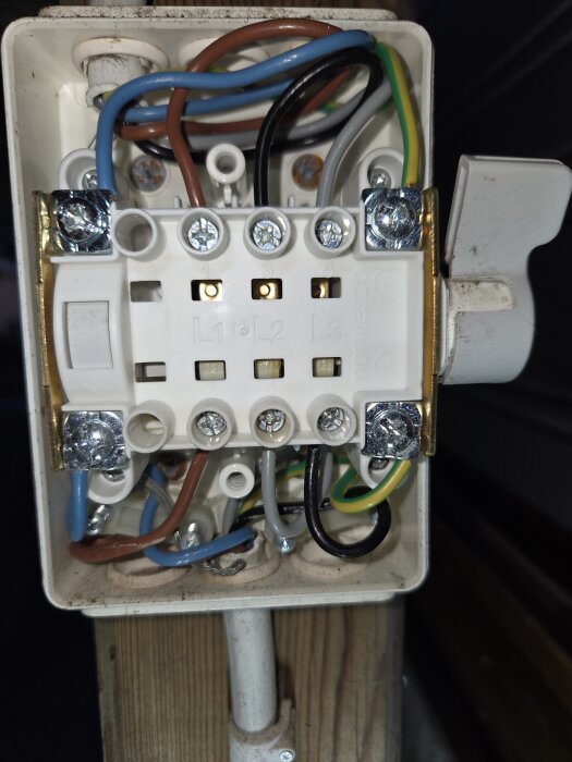 En elektrisk kopplingsdosa med synliga kablar och skruvar; spår av fukt kan ses under kabelingången upptill.
