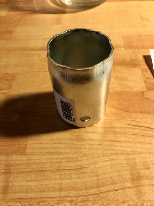 Metallhylsa med etikett på en träyta, används för att lossa ringen runt reglerkassetten på köksblandaren.