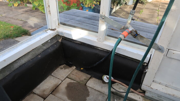 Vattenuttag med kopplade slangar i ett äldre uterum. Tätt intill syns en glasvägg och trädgårdsplattor.