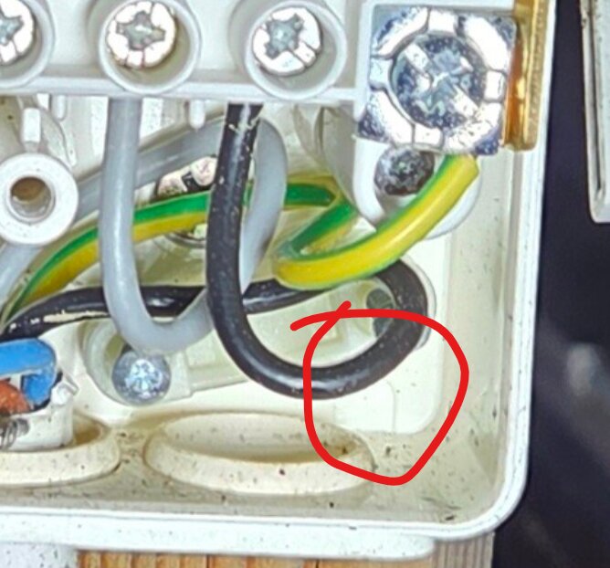 Elektrisk kapsling med kablar och skruvar, ett dräneringshål med fuktmarkeringar är inringat med röd markör.