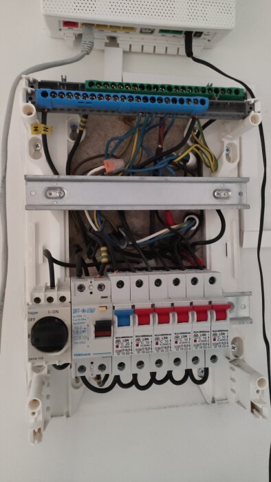 Öppen elcentral med blandade kablar synliga, flera kretsbrytare och en kopplingshatt monterad i en bostad.