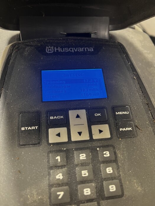 Närbild av en Husqvarna-batteridisplay som visar laddningsstatus och spänning på 17,2V. Knappar för start, meny och siffror syns.