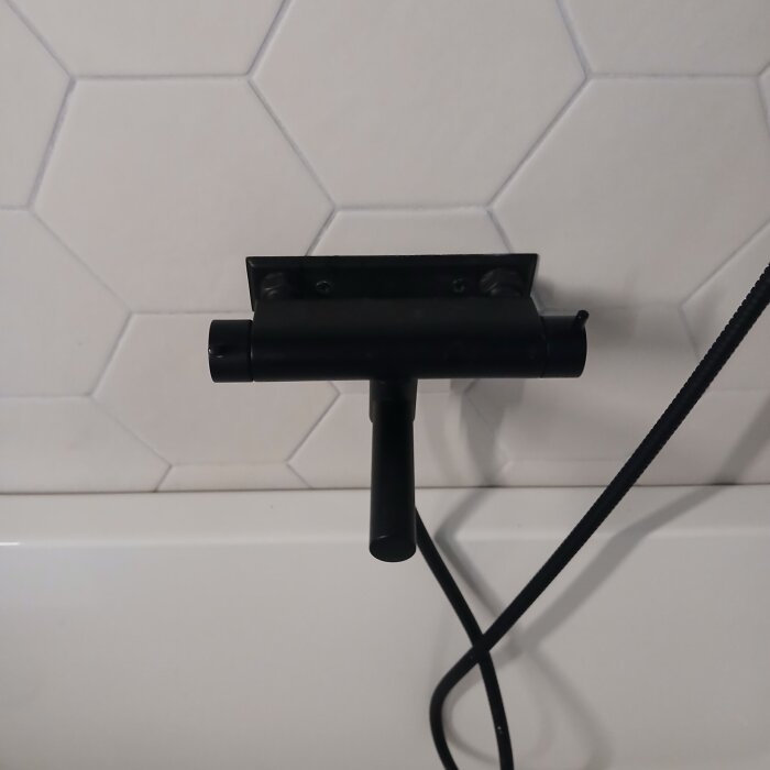 Svart duschblandare monterad direkt på kakel i badrum, med rör som går neråt mot badkaret.