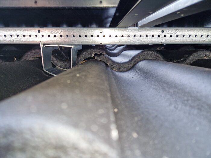 Takstruktur med takkrokar och springor mellan betongpannor, potentiell risk för läckage. Monteringsdetaljer synliga under solpaneler.