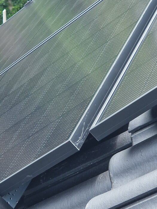 Solpaneler monterade på ett tak med betongpannor, synliga springor mellan pannorna och repor på panelerna.