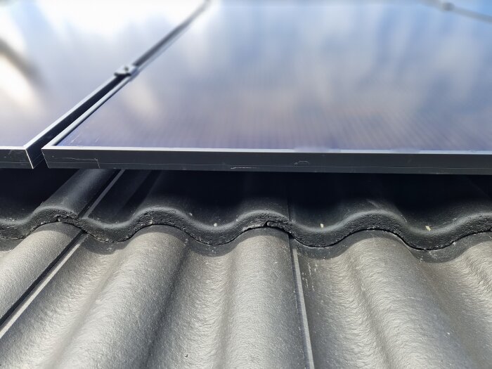 Solpaneler monterade på ett tak med betongpannor, med springa mellan pannorna synlig under panelerna.