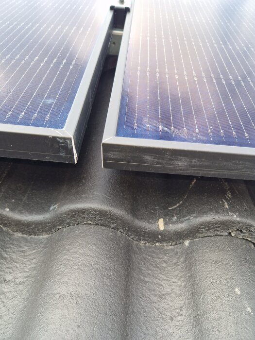 Närbild av solpaneler monterade på ett tak med synlig springa mellan två betongplattor, vilket kan indikera risk för läckage.