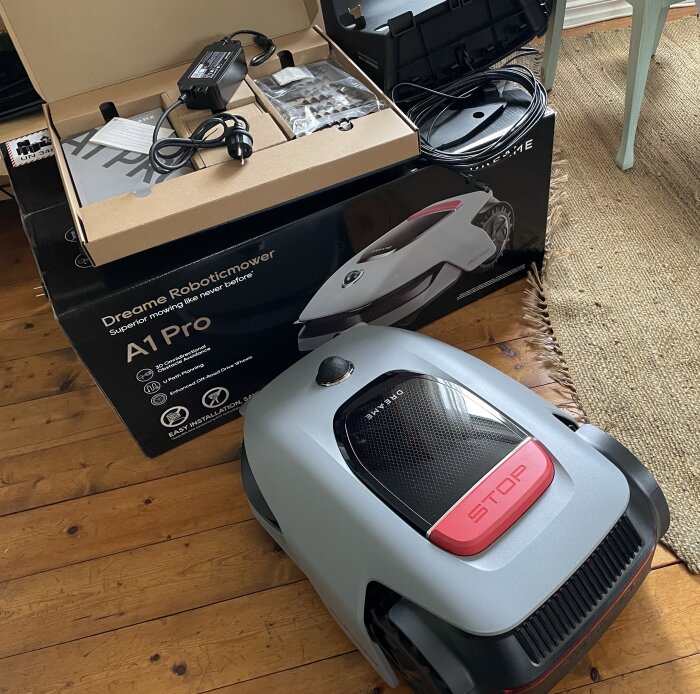 Förpackning och delvis uppackad robotgräsklippare Dreame A1 Pro syns i bilden på ett trägolv.