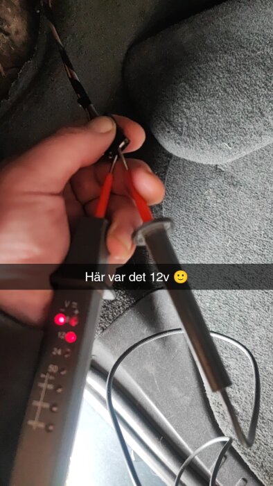 Hand som håller en spänningsprovare kopplad till 12v-kontakt i bilens bagageutrymme.