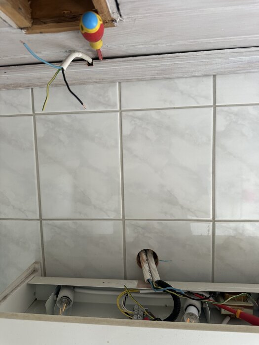Elektrisk installation med kort kabel framför kakelvägg, skruvmejsel och synliga ledningar.