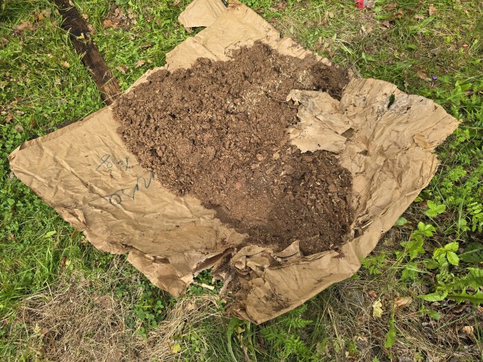 Brunt jordmaterial på brun papp, liggande på gräs. Möjligen är materialet kodynga, använt som isolering, enligt inlägg.