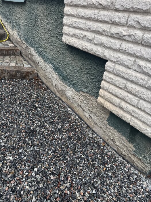 Fasad med ojämn yta, delvis lagad och målad i skogsgrönt, ovanför en gång av grus och stentrappa.