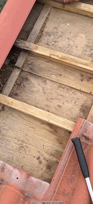 Närbild av ett tak med borttagna pannor som visar murknad plywood och en delvis synlig plåthake.