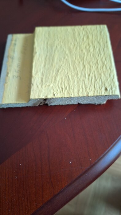 Närbild på en gulmålad träbit, troligtvis en Z-panel, med en "flärp" som är 35 mm bred, liggande på ett träbord.