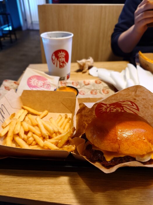Hamburgare och pommes frites serverade på en bricka vid Mister York med en dryck i bakgrunden.