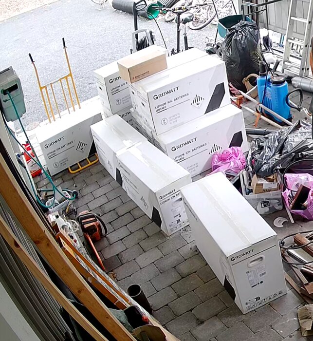Lådor märkta "Growatt Lithium Ion Batteries" i ett garage, omgivna av verktyg och andra föremål.