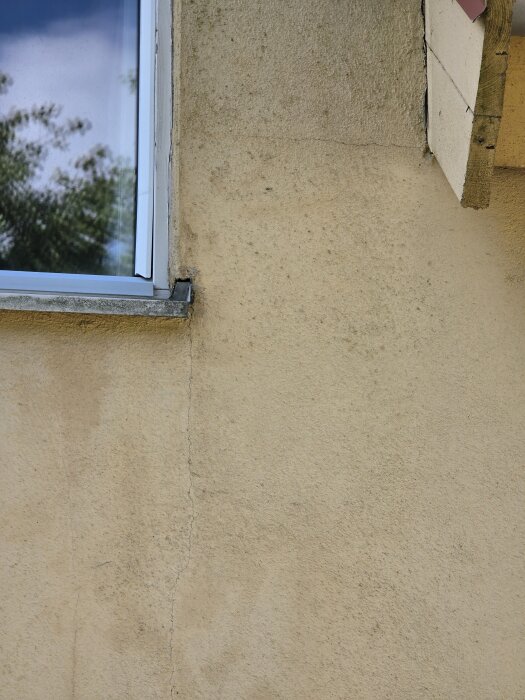 Putsfasad med fönster och spricka i väggen, foton för bygg- och renoveringsfråga om målning och fogning.
