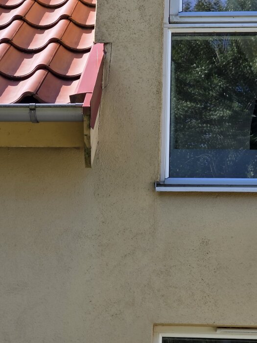Fasad av ett hus med puts och röda takpannor, små sprickor synliga nära fönster och tak, i samband med fråga om målning och fogning.