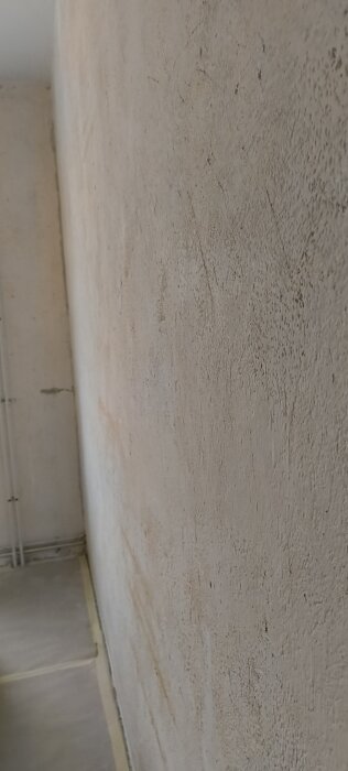 Förberedd vägg utan tapet, med synlig puts och limrester, redo för slipning och eventuell spackling.