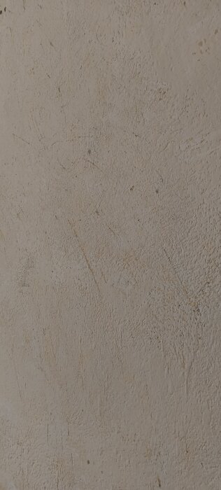 Närbild av vägg med borttagen tapet som avslöjar ojämn yta och eventuella puts- eller färgrester.