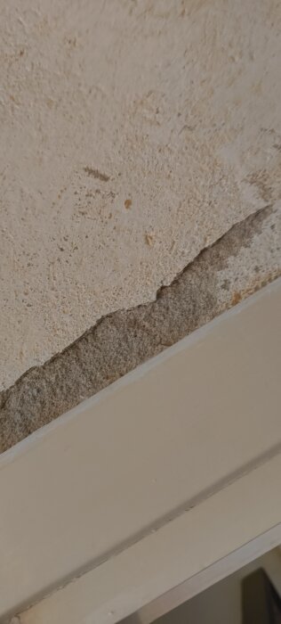 Närbild av vägg med borttagen tapet, visar misstänkt puts och eventuella gula limrester på en ojämn yta.