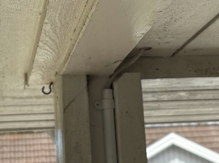 Vit takhörna med en synlig antennkabel i närbild, monterad längs ett hörn mellan tak och stolpe.