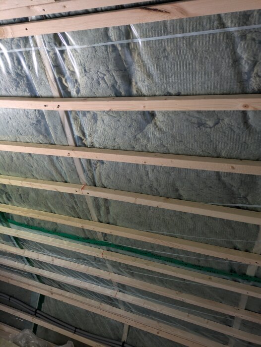 Isolering med stenull och plastfilm placerad mellan träreglar i ett takområde, en del av en renovering av ovanvåning.