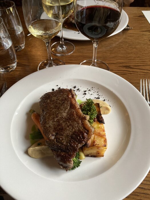 Middagstallrik med stekt kött, grönsaker, potatis och sås, serverad vid Mauritzbergs slott. Rött och vitt vin i glas.