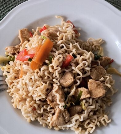 Wok med nudlar, kycklingbitar, morötter och paprika serverad på en vit tallrik.