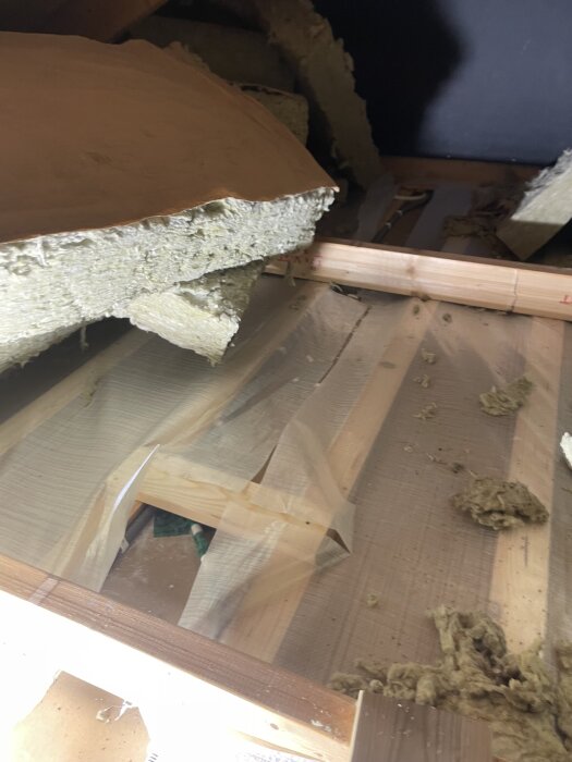 Skadad ångspärr på vind med synligt trästöd och isoleringsmaterial runt omkring, förberedd för reparation med ångspärrtejp.