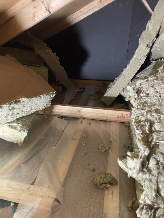 Vind med synlig ångspärr som skurits upp, omgiven av isolering och träreglar, med en sax och ångspärrtejp från TESA i närheten.