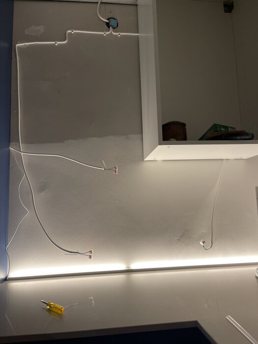 Kök under renovering med LED-ljusskena installerad under ett skåp. Tre kablar med Vago-klämmor synliga på väggen. En gul skruvmejsel på bänken.