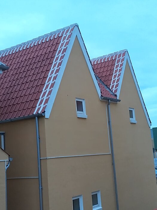 Vinklade tak med röd takpannor och vitmurade kanter på två gula byggnader.