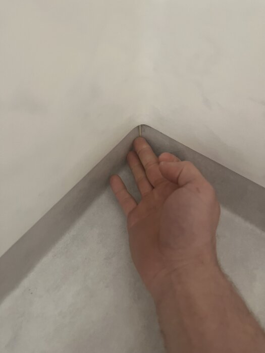 Hand visar hål i hörn av duschutrymme där golvmattan inte är tät, med tandpetare som indikerar djupet i hålrummet.