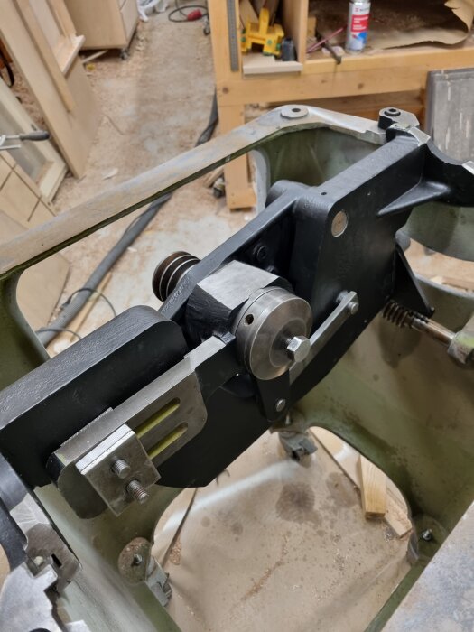 Monterad maskindel med nymålade motorfästen i ett verkstadsutrymme, omgiven av verktyg och träspån.