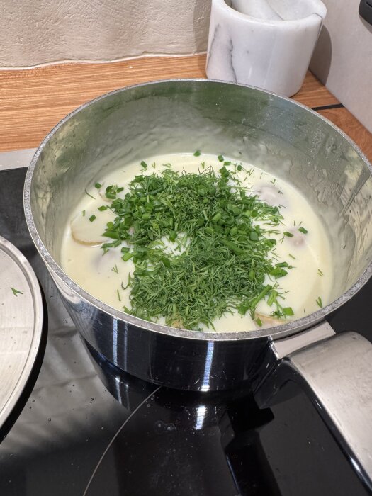 Kastrull med vit sås, fisk och hackade örter på spisen.