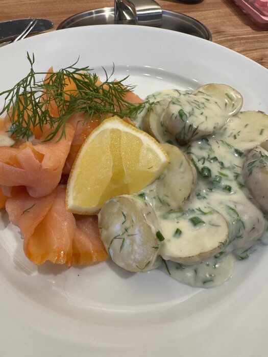 Tallrik med gravad lax, skivad potatis i dillsås, citronklyfta och dillkvistar.