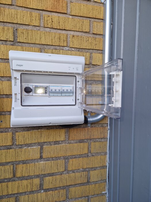 Elskåp på tegelvägg med öppen lucka, vattendroppar synliga på insidan av skåpet.