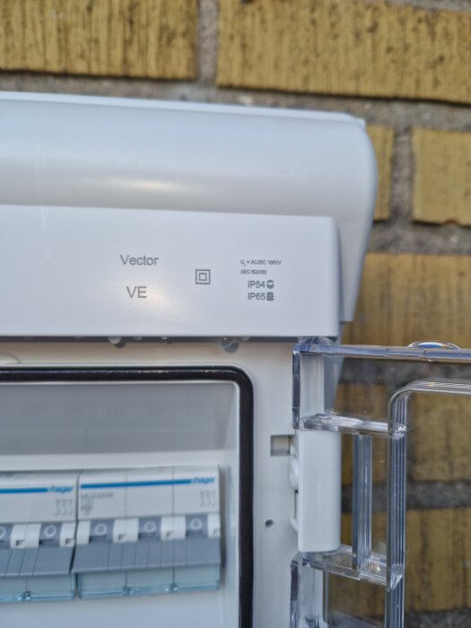 Inomhus elskåp med öppen lucka och vatten på brytarna, monterat på tegelvägg. Märkningsinformation synlig.