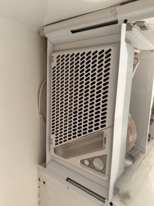Köksfläkt monterad i skåp med ventilationsgaller synligt från sidan; problem med passformen mot ventilationskanal i betongvägg.