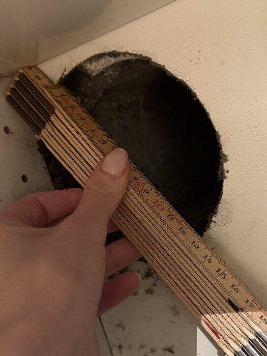 Håltagning i väggen med måttstock som mäter öppningens diameter, troligen kopplad till köksfläktens ventilationsproblem.
