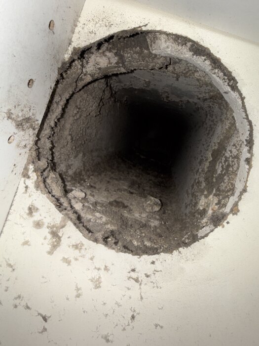 Ventilationskanal med damm och smuts runt öppningen i en betongvägg, visar springa mellan vägg och köksskåp.