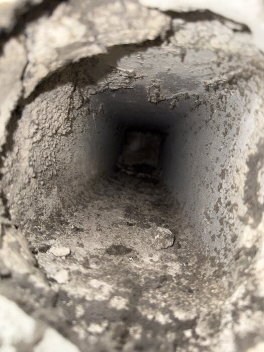 Sprucken och smutsig ventilationskanal i betong, med lösa delar inuti, skapad av springan mellan köksfläkten och väggen.